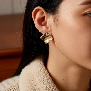 Close-up of geometric diamond earrings with 18k gold plating and ripple texture detail
