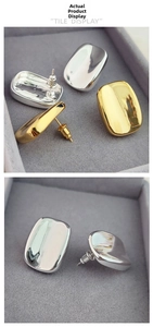 Detailed view of glossy gold and silver rounded rectangular stud earrings on velvet