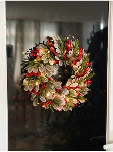 Close-up of 40cm Christmas wreath with red berries and warm LED lights on a window