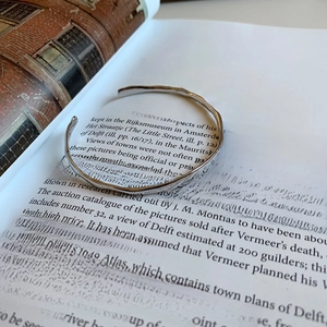 Macro detail of 925 sterling silver open bangle with organic hammered texture on a book
