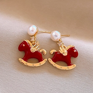 Detail of red rocking horse earring with zircon, pearl, and gold wings on beige fabric