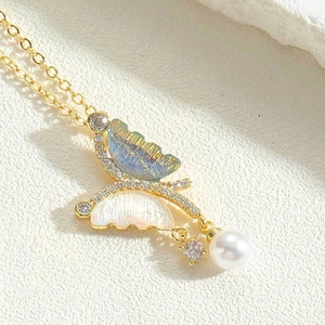 Macro shot of gold butterfly pendant with blue shell wings and white pearl drop
