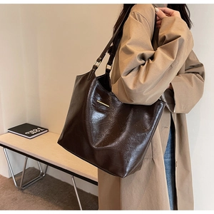 Detail view of dark brown faux leather tote bag with metal buckle on khaki trench coat