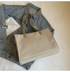 Detailed flat lay of beige canvas tote bag with PU straps on denim jacket background
