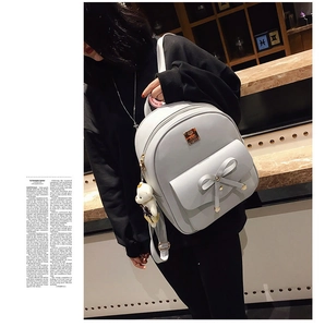 Close-up of white PU leather backpack featuring a large bow and cute teddy bear pendant