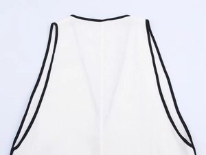 Flat lay of white knit vest with black contrast piping on V-neck and armholes