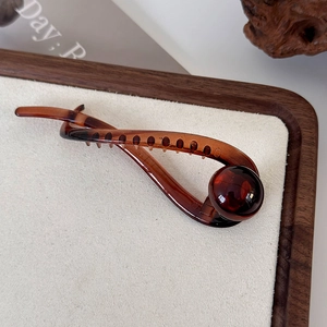 Detailed view of large brown twisted hair claw clip with ball bead on velvet stand