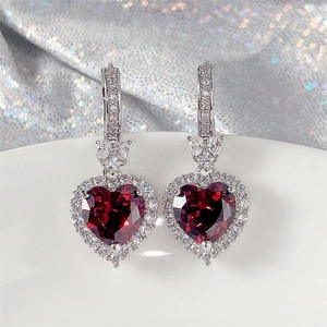 Macro detail of silver heart earrings with red gemstone and sparkling zirconia halo