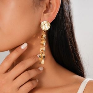 Detail of gold layered sequin tassel earrings with hammered metal texture on model
