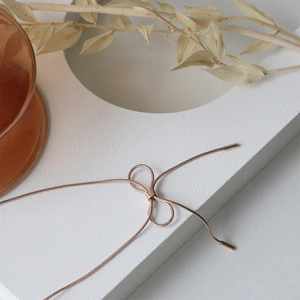 Macro detail of rose gold bow pendant on a delicate snake chain with an artistic background