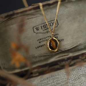 Tiger eye coffee bean pendant necklace with gold chain on a vintage jewelry box