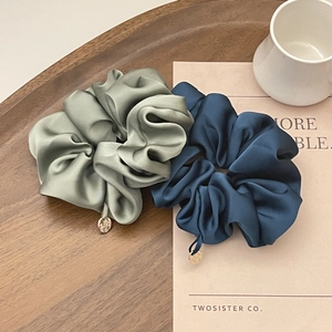 Close-up of premium satin scrunchies in olive green and navy blue with gold metal charms