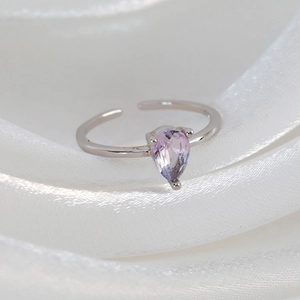 Close-up of silver ring with drop-shaped purple zircon on white silk background