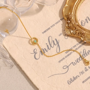 Detail of 18K gold plated chain with green natural stone pendant on textured paper