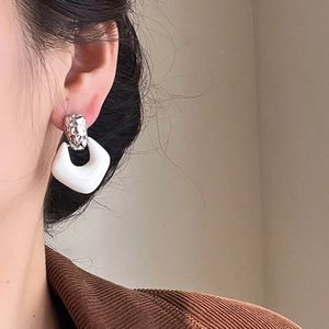 Close-up of minimalist silver twisted studs with white square pendants worn by a model