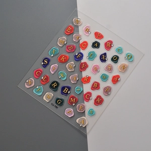 3D embossed nail art stickers with gold letter seals and rhinestone accents on grey background