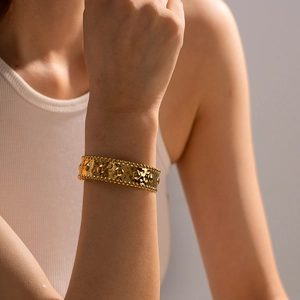 Close-up of a wide gold cuff bracelet featuring hammered texture and beaded edges