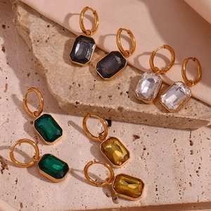 Detail view of gold-plated rectangular gemstone earrings on stone and pink satin fabric
