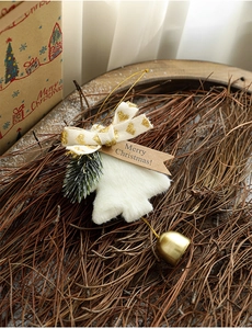 Close-up of plush Christmas pendant with golden bell and heart bow on pine needles