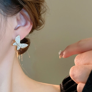Detail of elegant gold-plated butterfly stud earrings with white enamel on ear