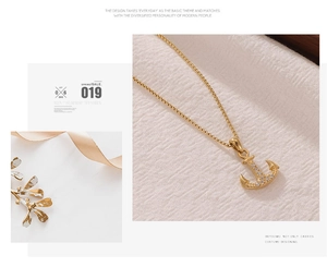 Détail du collier pendentif ancre dorée avec cristaux blancs sur tissu blanc