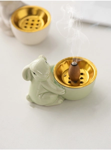 Macro view of a ceramic rabbit incense burner with a golden metal bowl and rising smoke