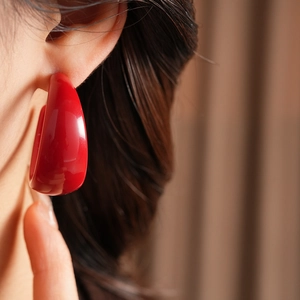 Close-up of red C-shaped resin earring on model featuring a glossy fashion finish