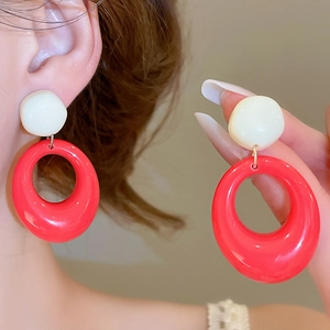 Détail de boucles d'oreilles pendantes ovales en résine rouge et crème sur mannequin