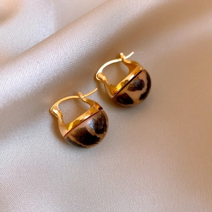 Detail view of vintage leopard print dome earrings on luxury champagne silk fabric