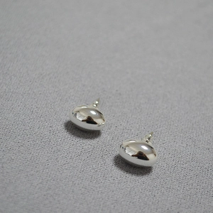 Macro detail of silver bean stud earrings with polished mirror finish on textured fabric