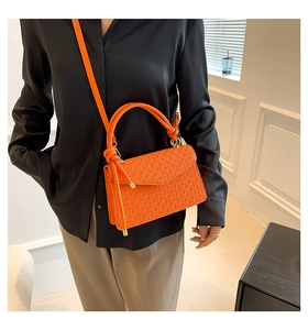 Detail van de geweven textuur en knoophendel op een feloranje lederen crossbodytas