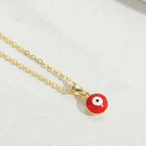 Detail of red evil eye pendant with golden chain on white leather texture background