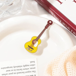 Detailed view of a yellow acrylic guitar hair clip featuring the Mark lettering on a plate