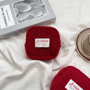 Detail of red fleece and corduroy coin purses with embroidered brand tags on soft fabric