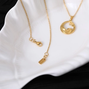 Detail of gold wave pendant necklace with lobster clasp and logo tag in a shell tray