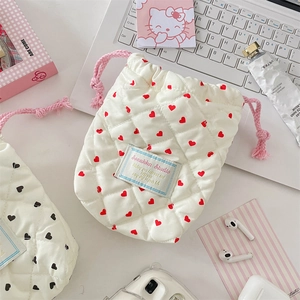 Close-up of white quilted drawstring pouch with red hearts next to a laptop and headphones