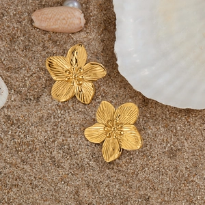 Detailed macro shot of gold flower earrings with brushed texture on a sandy beach background