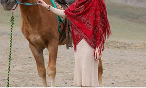 Scialle rosso tipo cashmere con motivo paisley e nappe mostrato in un ambiente desertico
