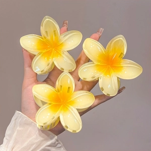 Detailed view of three acrylic frangipani hair claws with yellow gradient petals