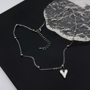 Polished silver heart pendant necklace on minimalist beaded chain over crystal glass