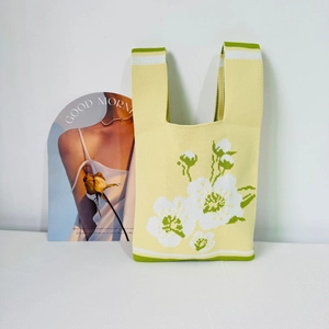 Detail showing knitted texture and white flower patterns on a yellow tote bag