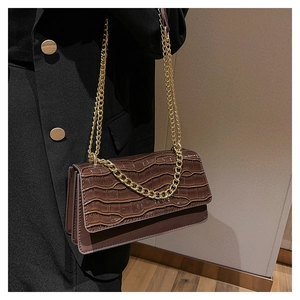 Détail du sac bandoulière marron motif croco avec chaîne dorée sur un manteau noir