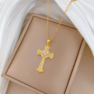 Dettaglio della collana a croce dorata con strass lucidi su sfondo in seta bianca
