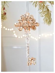 Detail of clear acrylic snowflake ornament with gold sequins hanging on a pine branch