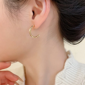 Close-up of elegant gold twisted C-shape hoop earrings worn by a model for a luxury look