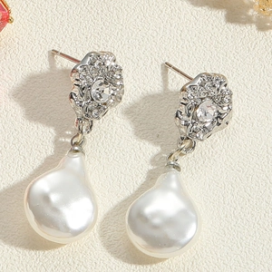 Close-up of baroque pearl earrings with crystal floral studs on beige texture