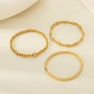 Detailed view of three 18K gold plated beaded bracelets on a neutral minimalist background