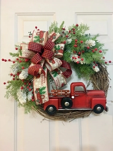 Detail of Christmas wreath with red truck model, pine needles and berries on white door