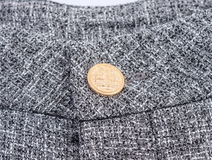Macro detail of grey tweed fabric texture with decorative gold embossed button
