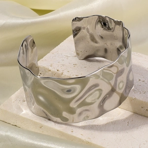 Macro shot of silver wave textured stainless steel cuff on white stone pedestals